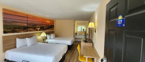 Habitación de hotel con dos camas, un escritorio, una silla, un cuadro en la pared y una puerta con un número.