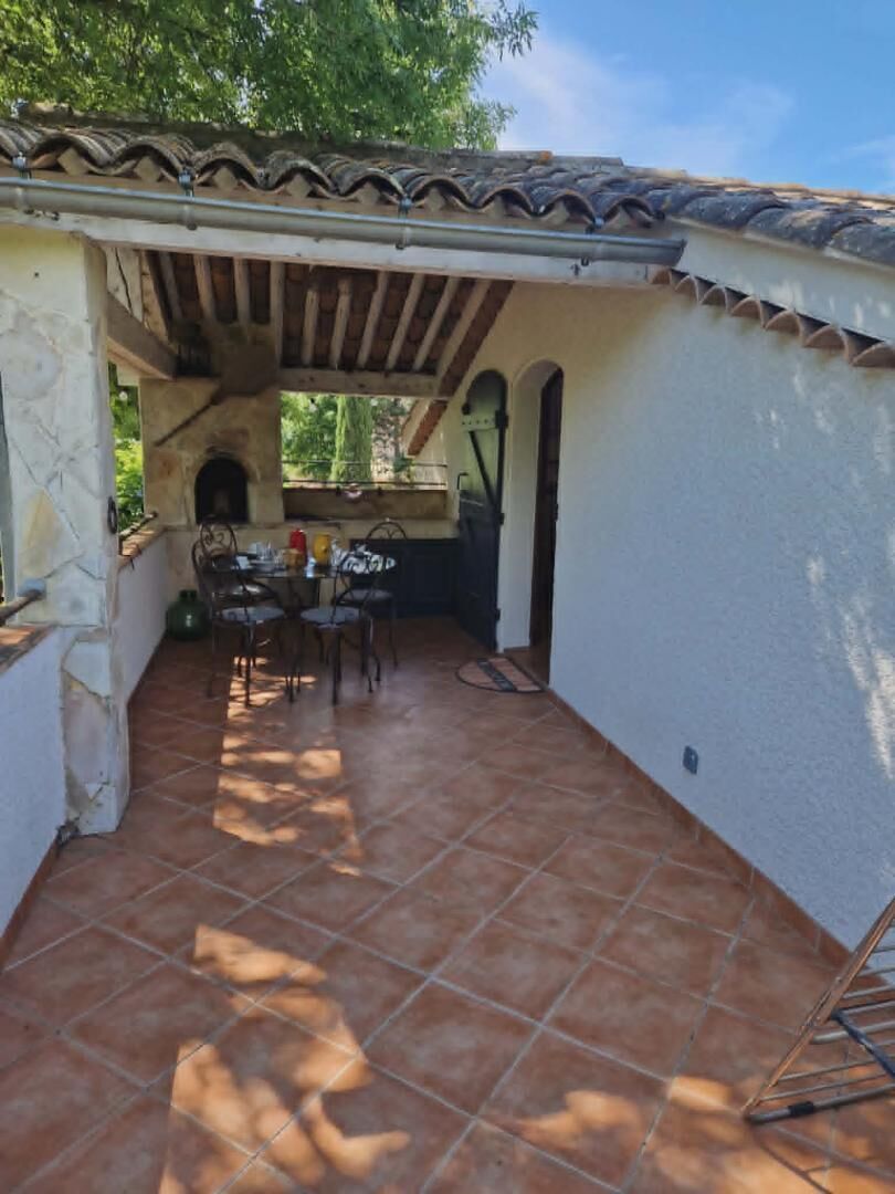 Une terrasse extérieure avec un sol carrelé, une table entourée de chaises et une structure en forme de pergola.