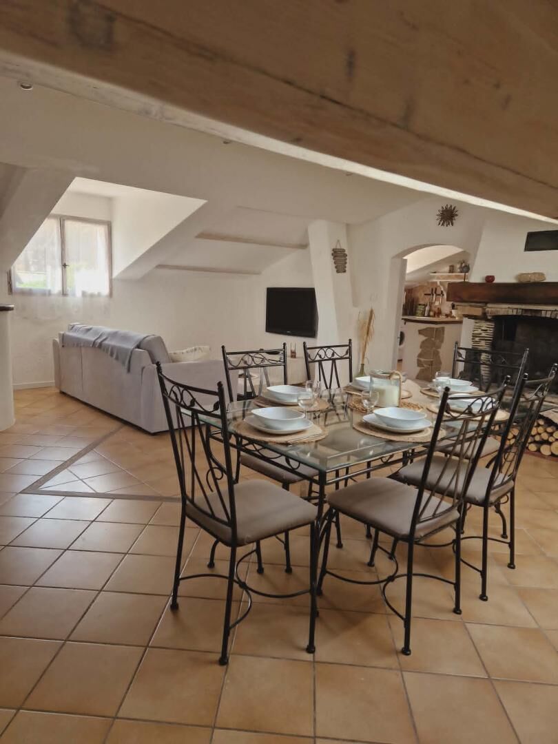 Een eetruimte met een tafel gedekt voor zes personen, omringd door stoelen, in een kamer met een schuine kap en een open haard.
