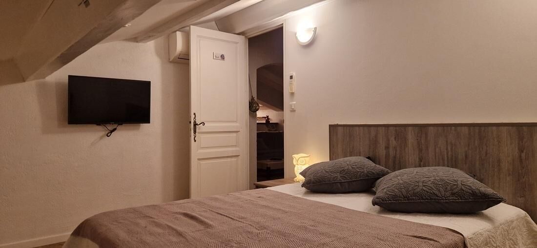 Une chambre à coucher avec un lit, un téléviseur fixé au mur, une porte et une lampe de chevet.
