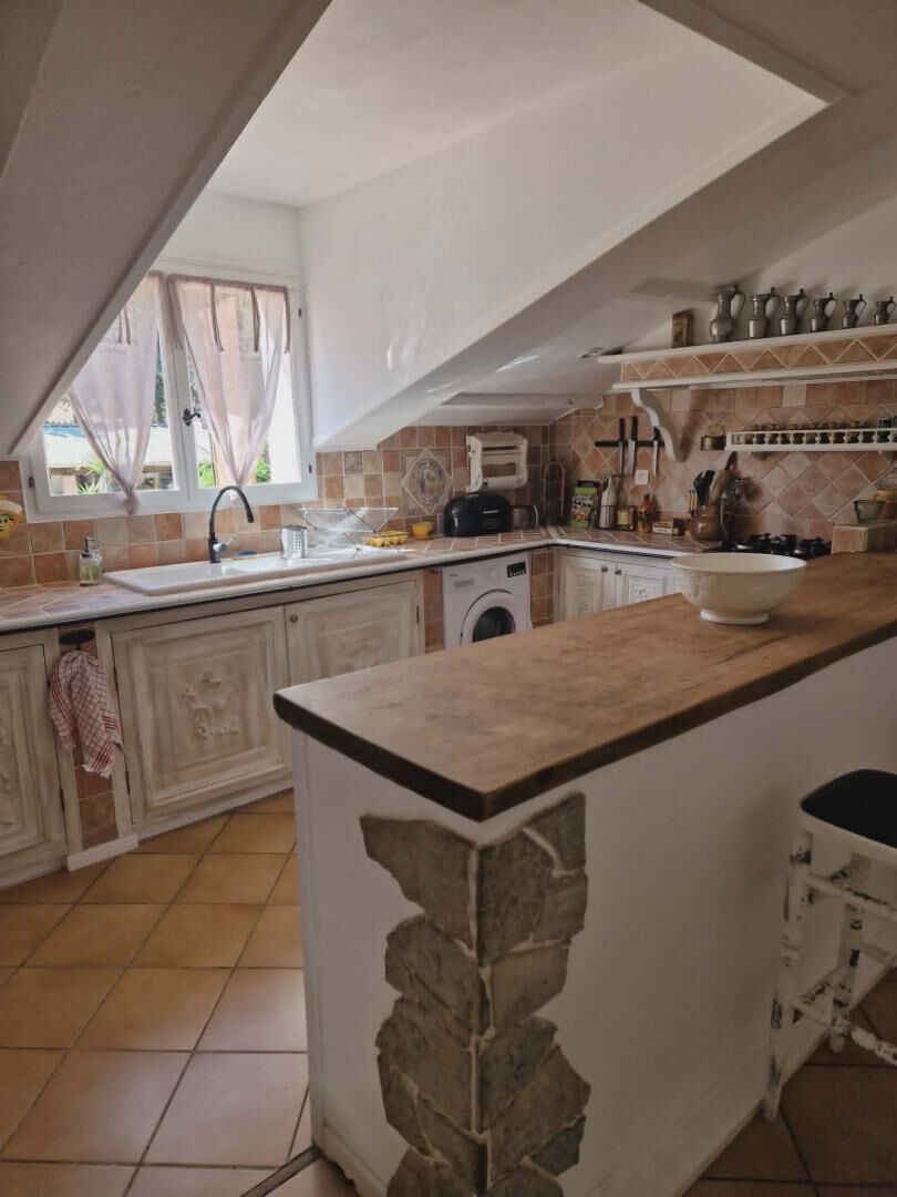 Une cuisine avec un mur d’accent en pierre, un four encastré et une fenêtre ornée de rideaux légers.