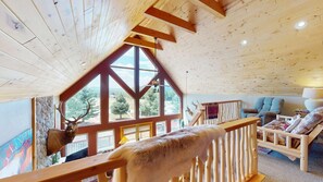 A cabin interior with a wooden ceiling, a balcony with a deer head decoration, and a view of the outdoors. - Master ensuite | Wood burning fireplace | Bike & Ski Gear Storage | Byrd's Nest (Angel Fire)