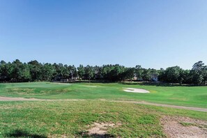 A golf course with a clear sky, a well-maintained green, sand bunkers, and a row of trees in the background. - Fairway View on Isabella Golf Course (Hot Springs Village)