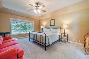 A bedroom with a bed, two bedside lamps, a ceiling fan, a window, and a red chair. - Fairway View on Isabella Golf Course (Hot Springs Village)