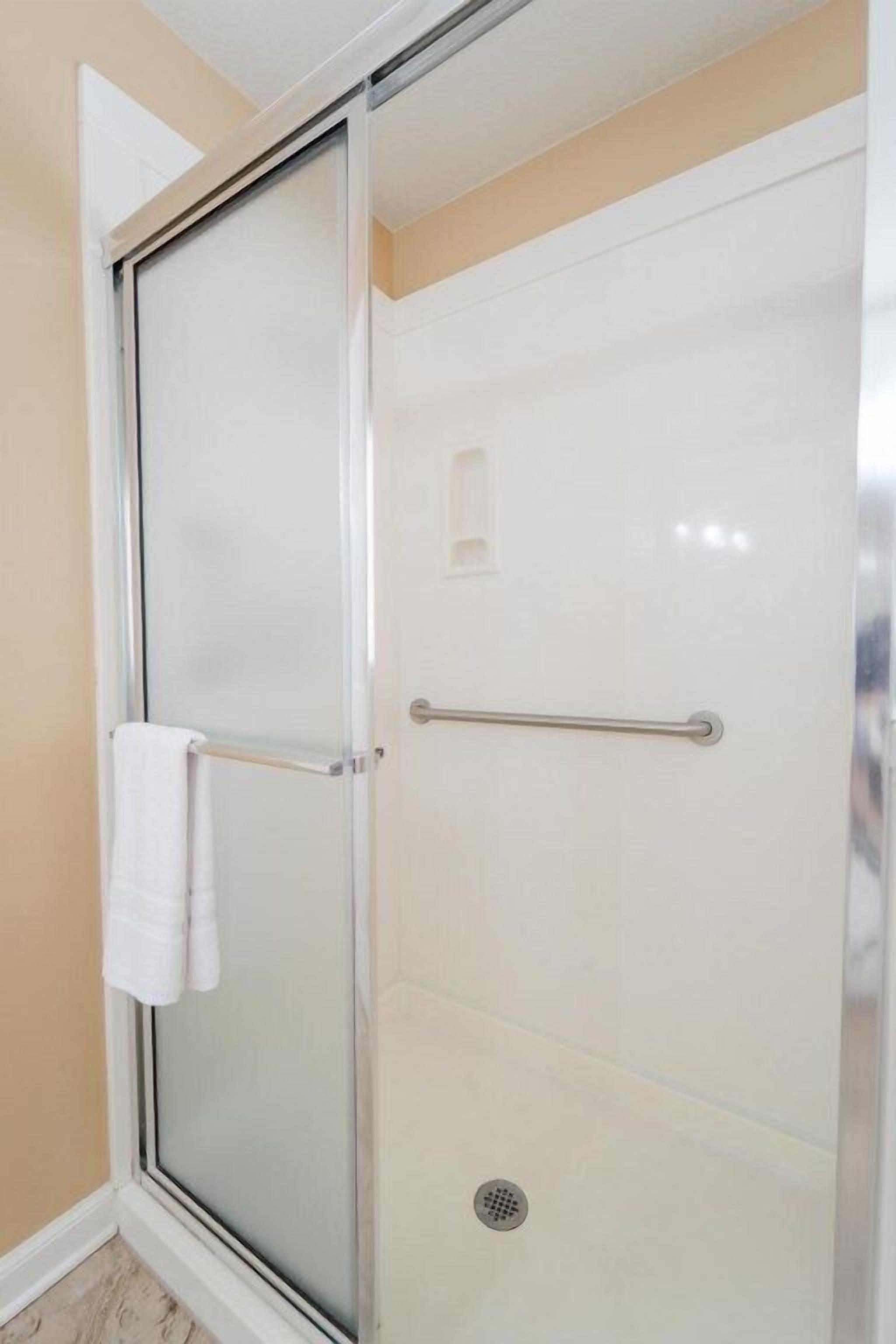 A glass-enclosed shower with a white towel on the door handle and a metal grab bar.