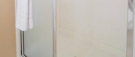 A glass-enclosed shower with a white towel on the door handle and a metal grab bar.