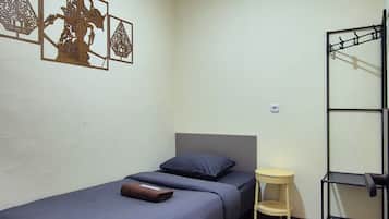 Une chambre avec un lit simple, une tête de lit, une petite table de chevet, un climatiseur fixé au mur et des œuvres d’art décoratives accrochées au mur.