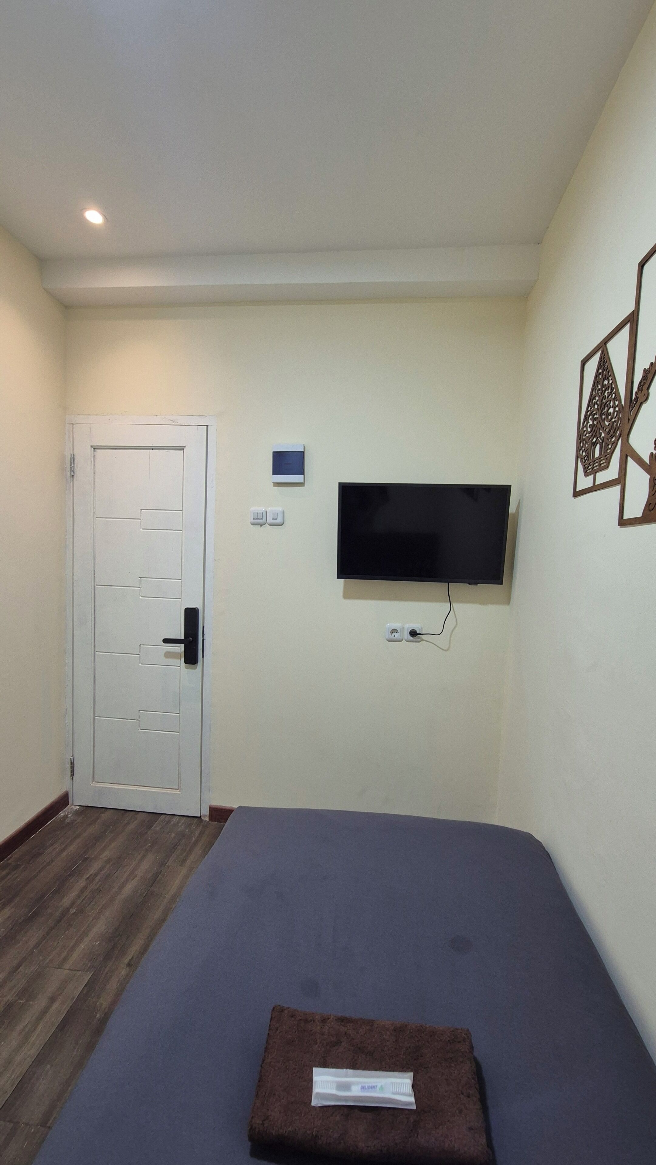 Une pièce comprenant un lit, un téléviseur fixé au mur, une porte et un luminaire fixé au mur.