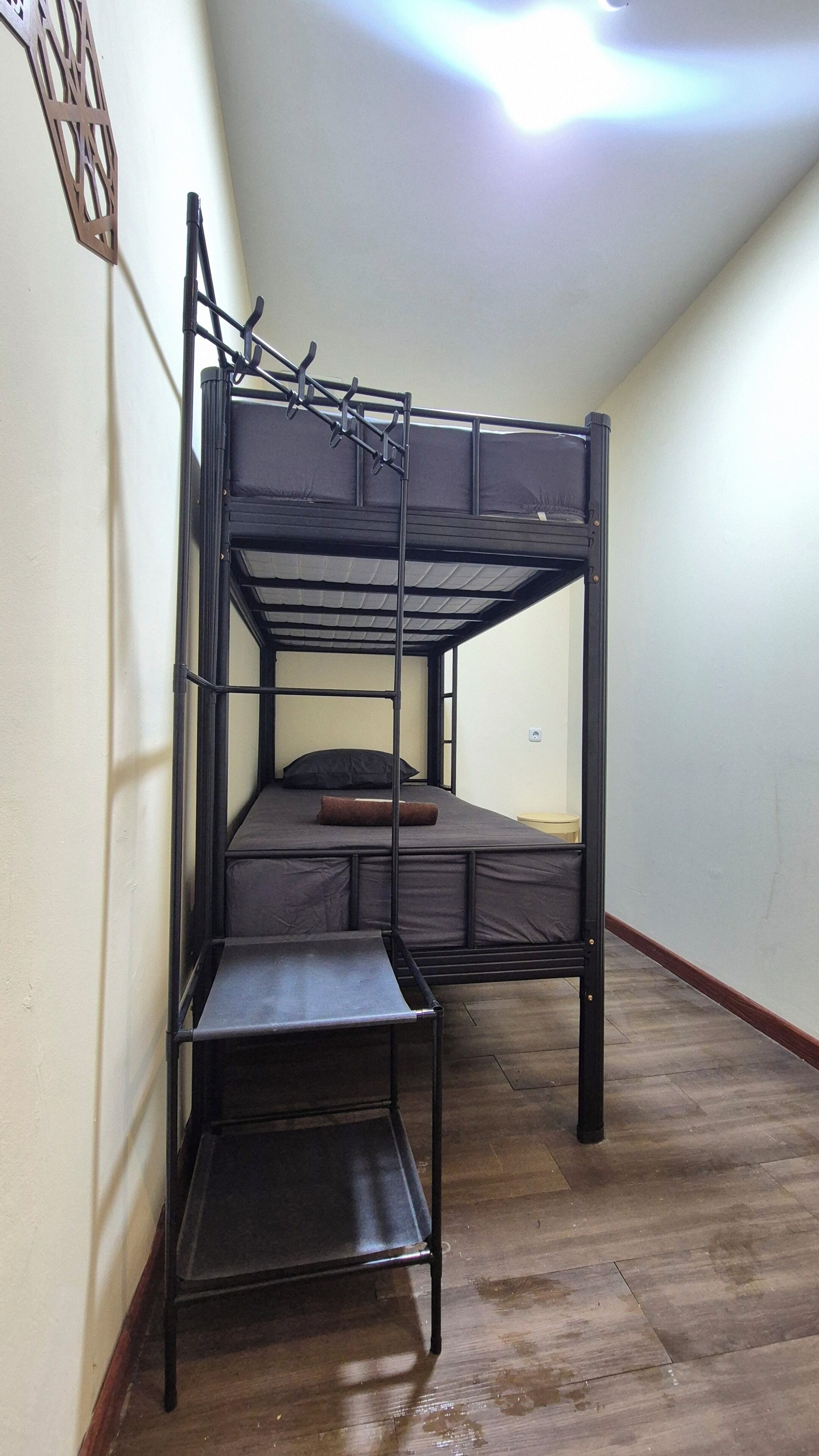 A bunk bed with a pull-out desk in a room with wooden flooring and a light fixture on the ceiling.