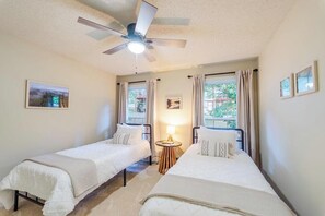 A hotel room with two single beds, a ceiling fan, a small table with a lamp, and a window with curtains. - Goldies Birdie Roost (Hot Springs Village)