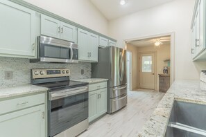 A modern kitchen with stainless steel appliances, light green cabinets, and a marble countertop. - Pepper's Pines and Putts, on Isabella golf course (Hot Springs Village)