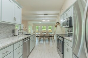 A modern kitchen with white cabinetry, a central island with seating, and stainless steel appliances. - Pepper's Pines and Putts, on Isabella golf course (Hot Springs Village)