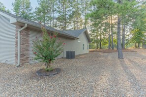 A house with a gravel driveway, a small tree with red flowers, and a metal air conditioning unit. - Pepper's Pines and Putts, on Isabella golf course (Hot Springs Village)