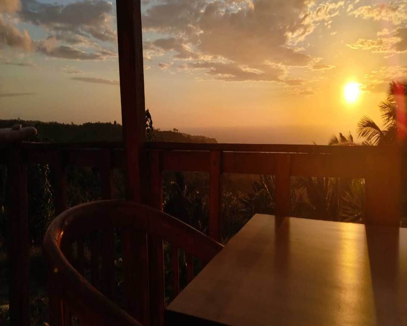 A wooden table and chair with a view of the sunset over a landscape.