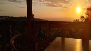 A wooden table and chair with a view of the sunset over a landscape.