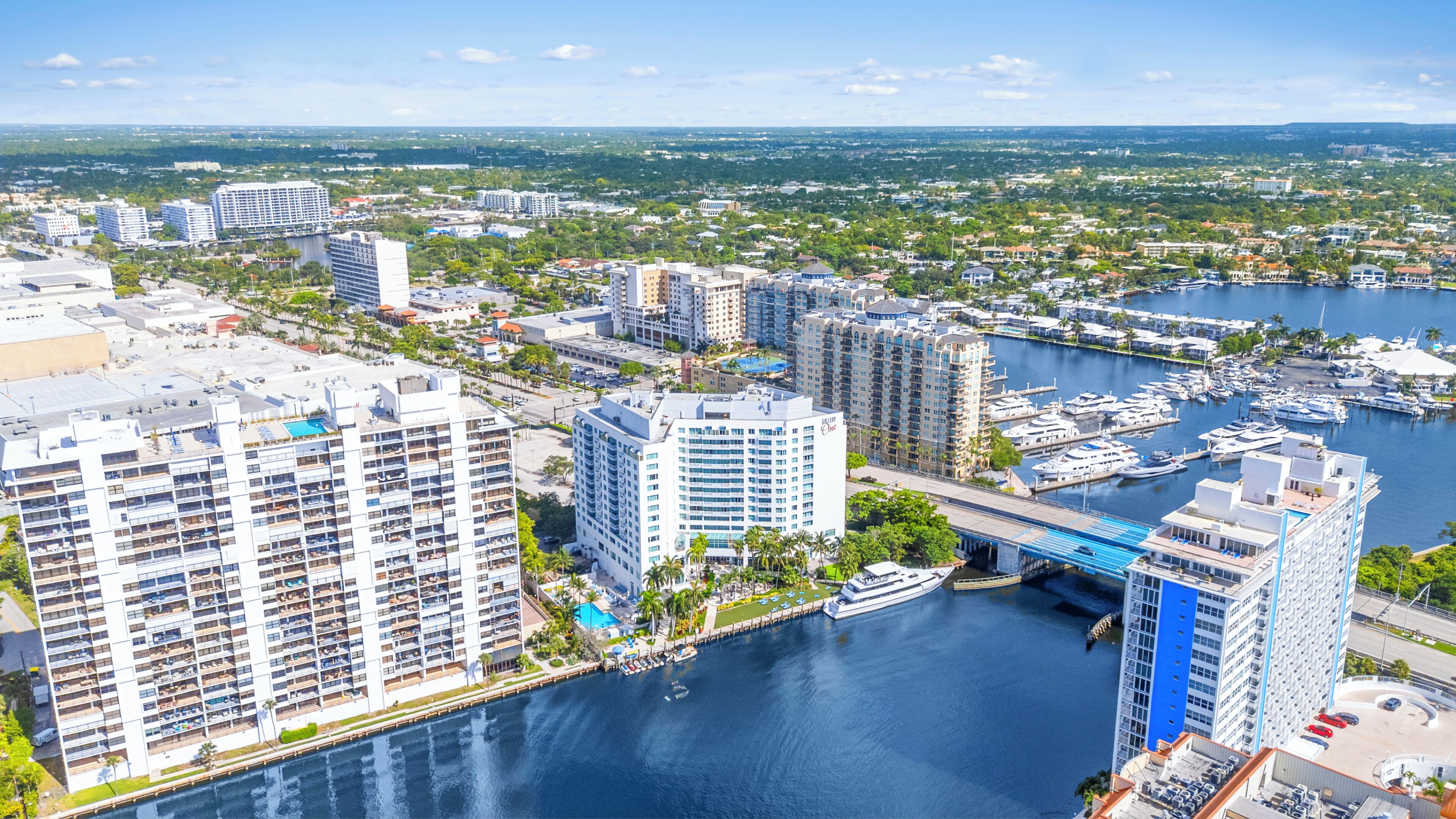 A high-rise hotel with multiple floors, a marina with boats, and a bridge connecting the buildings.