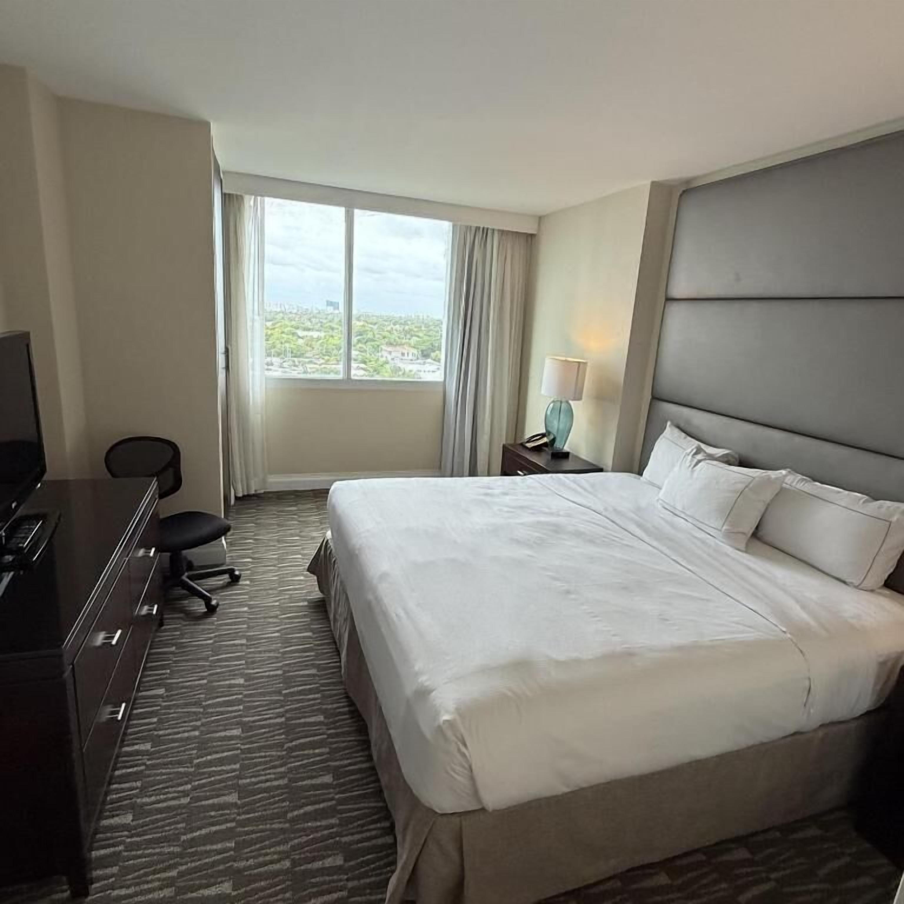A hotel room with a large bed, a desk with a chair, a television, and a window with curtains.
