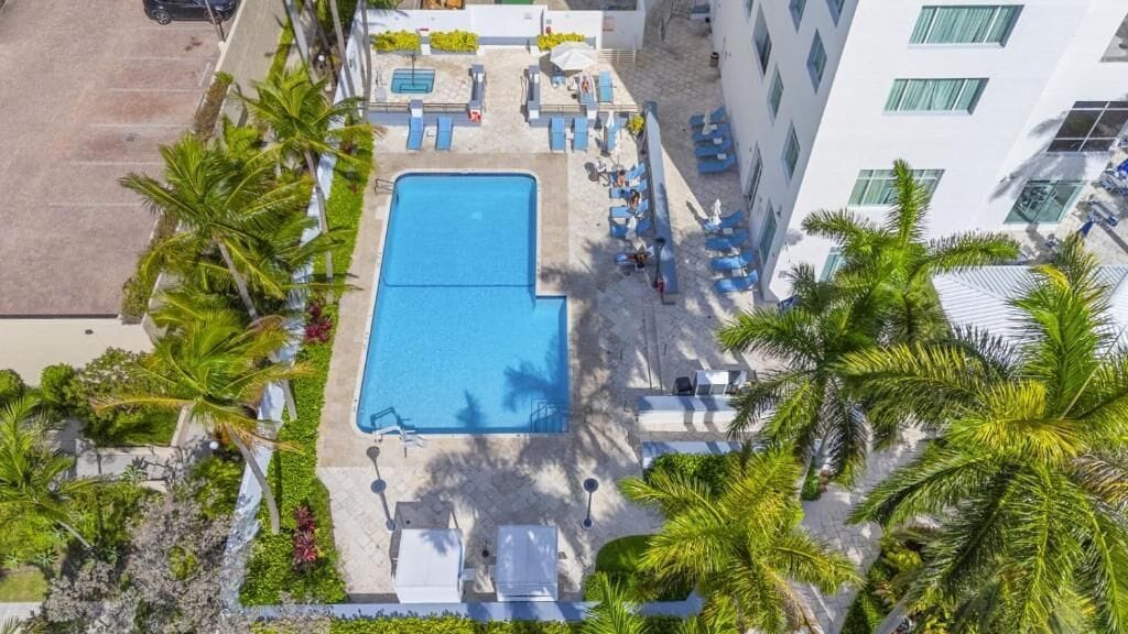 An aerial view of a hotel with a swimming pool, sun loungers, and palm trees.