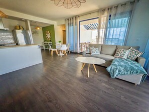A modern living room with a sofa, a dining table with chairs, and a kitchen area with a refrigerator. - Teani Skyline | Downtown Papeete • Terrace • Moorea View • A/C • Parking (Papeete)