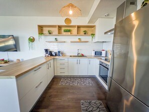 A modern kitchen with a built-in refrigerator, microwave, and oven. There are wooden cabinets, a wooden countertop, and a hanging light fixture. - Teani Skyline | Downtown Papeete • Terrace • Moorea View • A/C • Parking (Papeete)