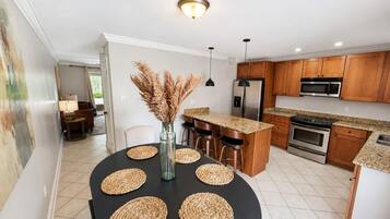 Una cocina moderna con armarios de madera, una isla central y un comedor con mesa negra y individuales tejidos.