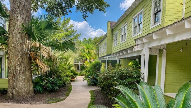 A pathway flanked by lush greenery and a green building with multiple windows.