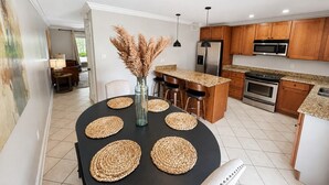 A modern kitchen with wooden cabinets, a central island, and a dining area with a black table and woven placemats.