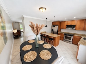 A modern kitchen with wooden cabinets, a central island, and a dining area with a black table and woven placemats.