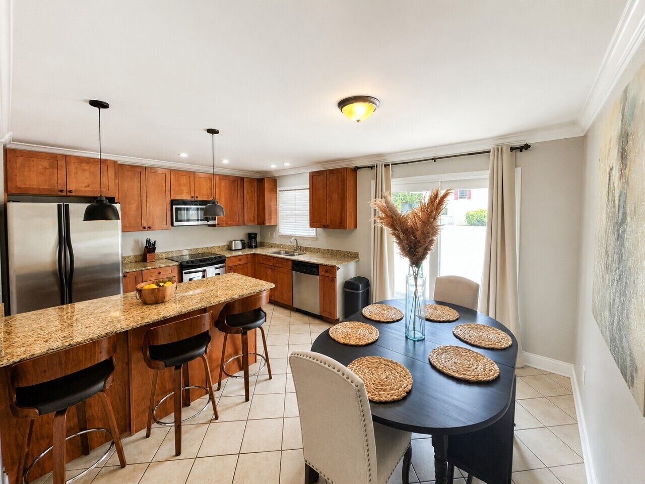 A modern kitchen with wooden cabinets, stainless steel appliances, and a dining area with a round table and bar stools.