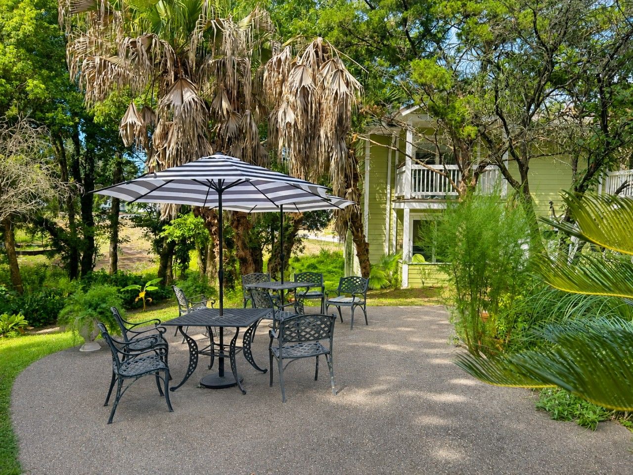 An outdoor patio with a table and chairs, surrounded by lush greenery and a hanging plant.