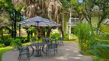 An outdoor patio with a table and chairs, surrounded by lush greenery and a hanging plant.