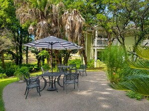 An outdoor patio with a table and chairs, surrounded by lush greenery and a hanging plant.