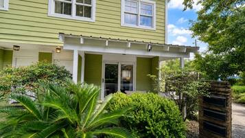A two-story house with a porch, a garage door, and a small garden with palm trees.