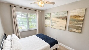 A bedroom with a bed, a ceiling fan, and artwork on the wall.