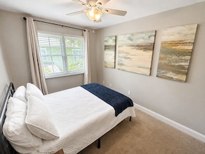 A bedroom with a bed, a ceiling fan, and artwork on the wall.