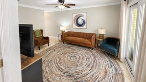 A living room with a brown sofa, a blue armchair, a patterned rug, and a ceiling fan.