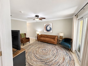 A living room with a brown sofa, a blue armchair, a patterned rug, and a ceiling fan.