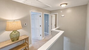 A hallway with a lamp, a console table, and a white railing.