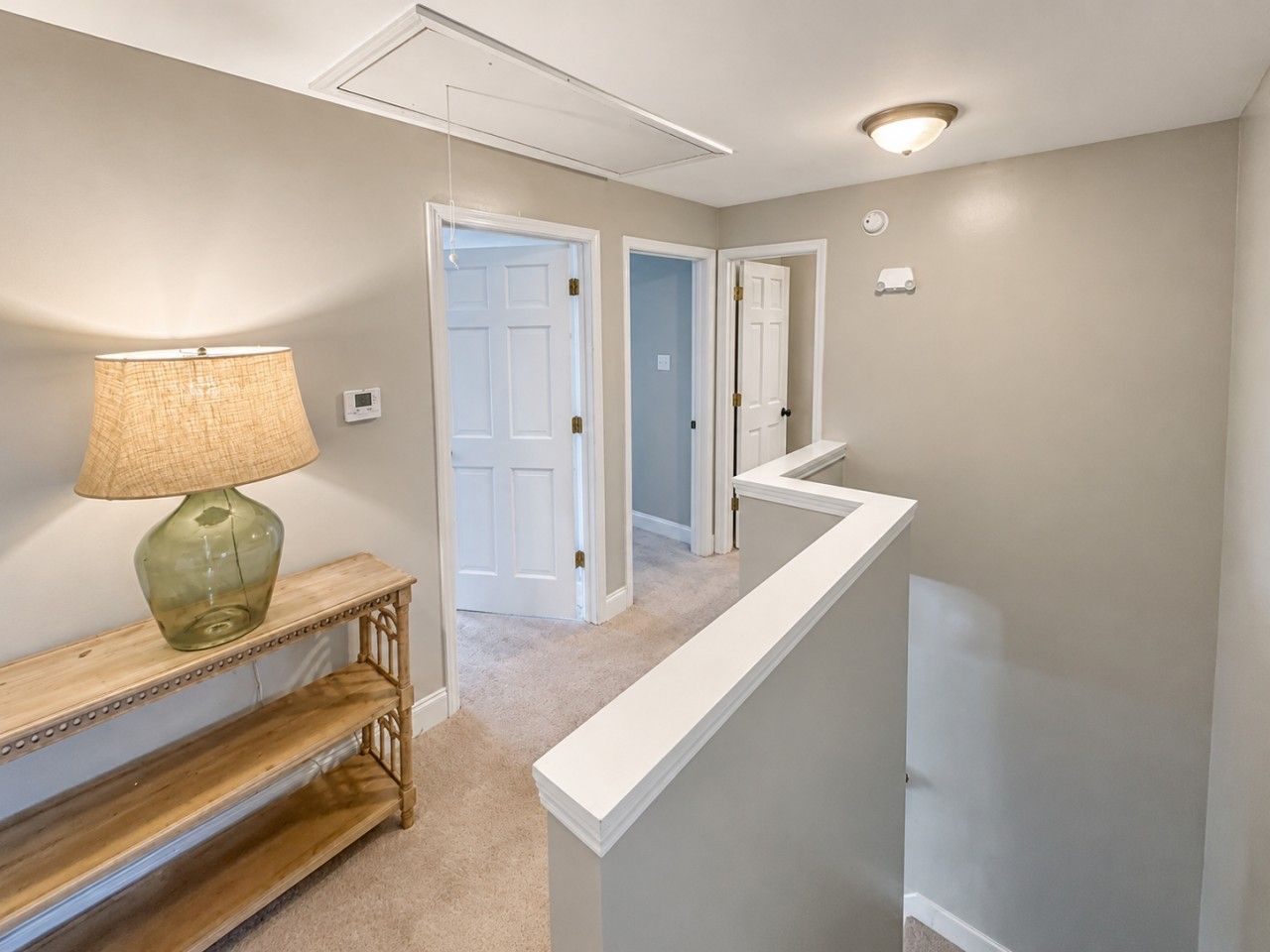 A hallway with a lamp, a console table, and a white railing.
