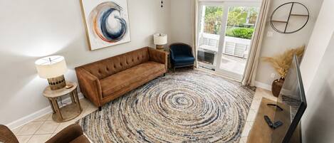 A living room with a brown sofa, a blue chair, a round rug, a ceiling fan, and a TV stand.