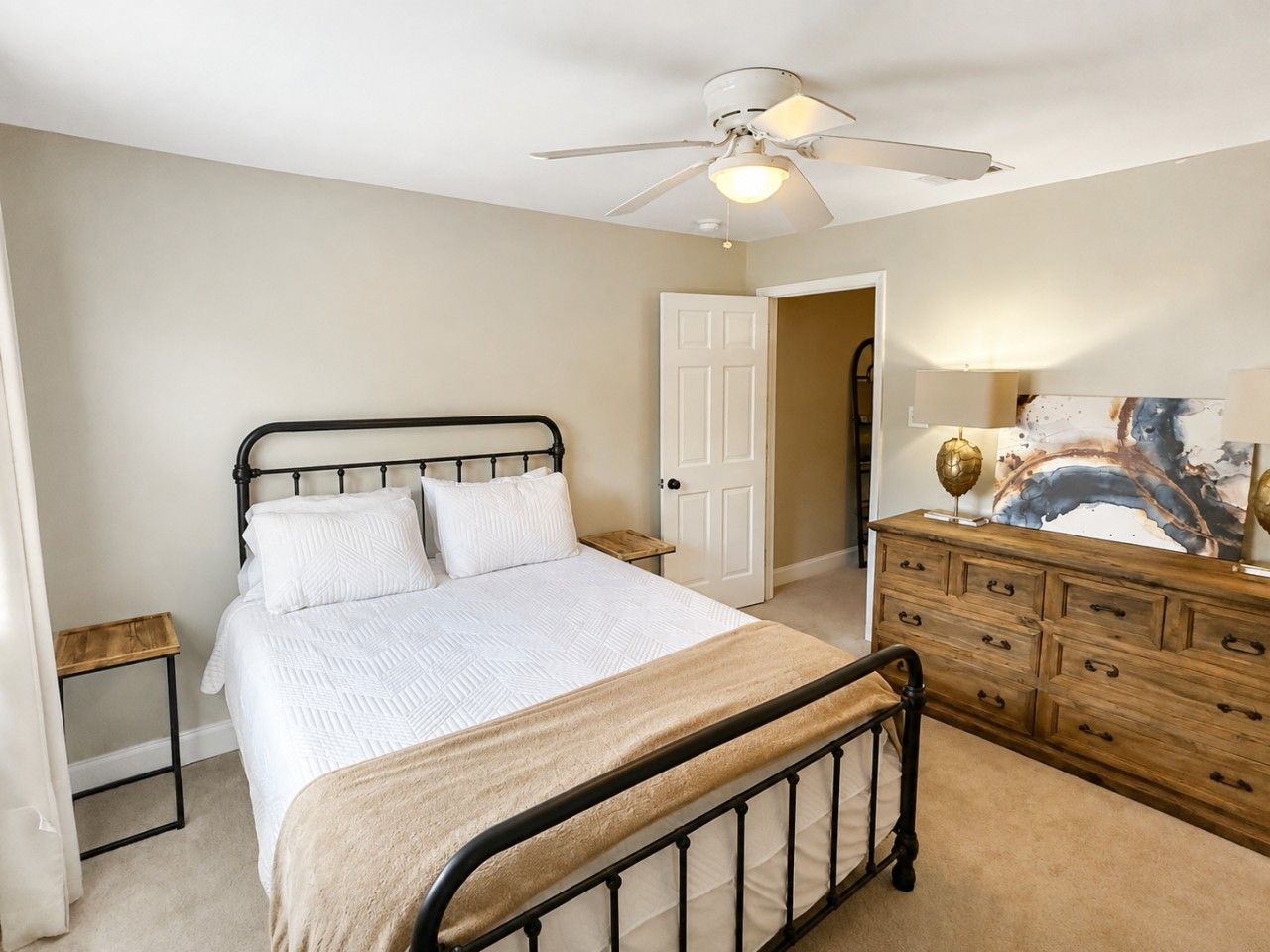 A bedroom with a bed, a dresser, a nightstand, a ceiling fan, and a door.