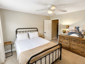 A bedroom with a bed, a dresser, a nightstand, a ceiling fan, and a door.