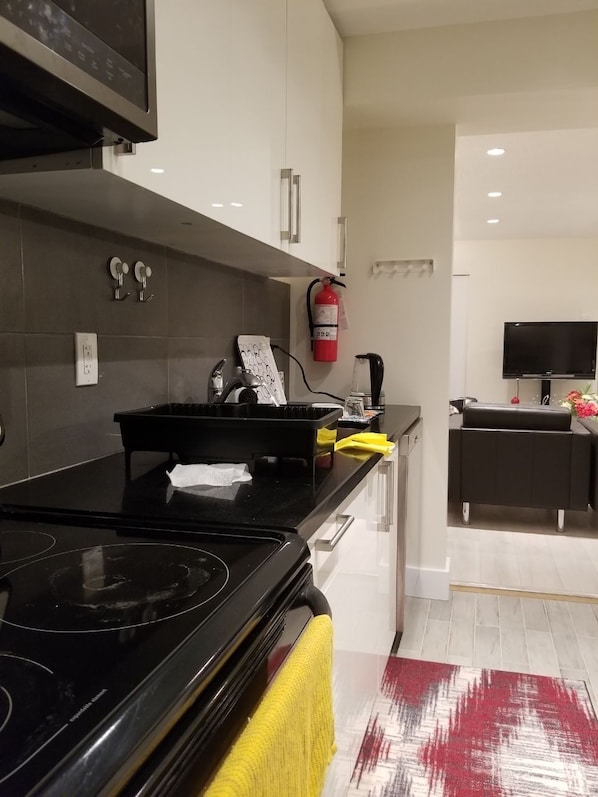 A modern kitchen with a black stove, white cabinets, and a yellow towel on the counter. - North Van Escape: Private 2BR Basement Near Grouse & Capilano Bridge (North Vancouver)