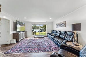 A living room with a large window, a black leather sofa, a patterned rug, and a mounted television.