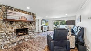 A modern living room with a stone fireplace, a black leather sofa, and a flat-screen TV mounted on the wall. - All about that Bass lake house on beautiful lay lake (Shelby)