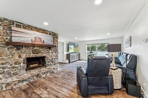 A modern living room with a stone fireplace, a black leather sofa, and a flat-screen TV mounted on the wall. - All about that Bass lake house on beautiful lay lake (Shelby)