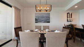 Un coin repas avec une table dressée pour quatre personnes, un lustre, un tableau représentant la mer et une vue sur l’extérieur.