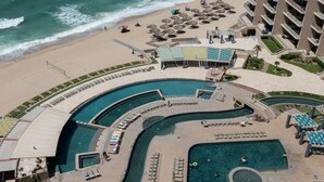 Ein Resort mit einem großen, gebogenen Pool, einem Strandabschnitt mit Sonnenschirmen und einem Gebäude mit Balkonen.