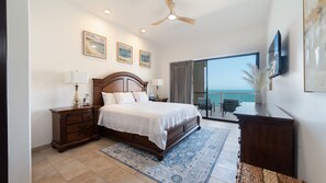 A bedroom with a large bed, a nightstand, a dresser, a ceiling fan, and a view of the ocean through a sliding glass door. - Las Palomas Phase II Coronado 1201 Exceptional Oceanfront 2BR 2BA Unit. (Puerto Peñasco)