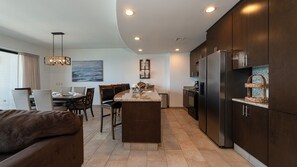 A modern kitchen with dark cabinetry, a central island, and a dining area with chairs and a table. - Las Palomas Phase II Coronado 1201 Exceptional Oceanfront 2BR 2BA Unit. (Puerto Peñasco)